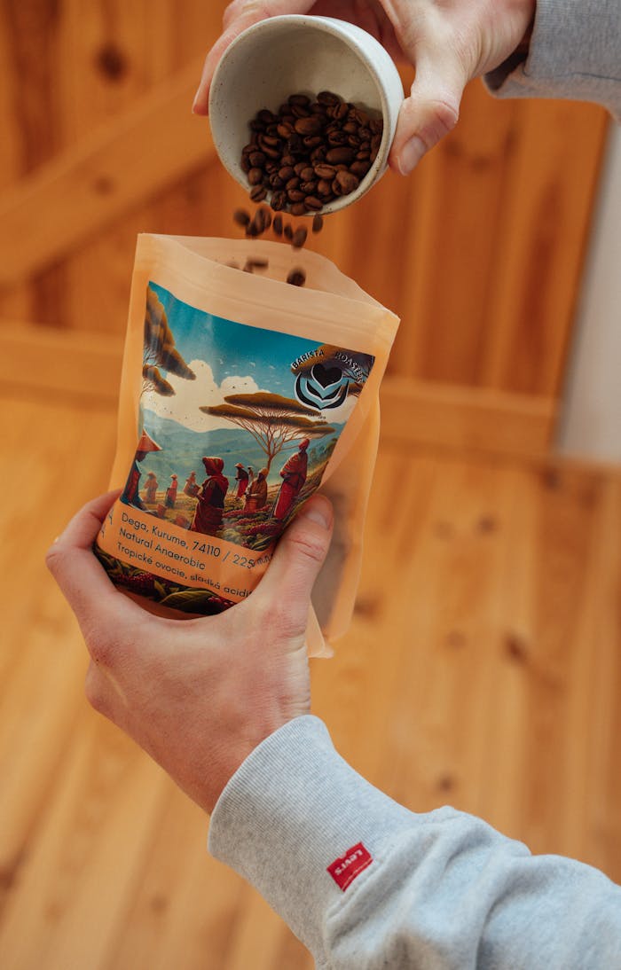 Hands pouring coffee beans into Ethiopian coffee blend package indoors on a wooden surface.